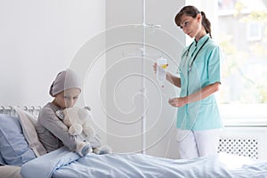 Doctor with drip visiting sad sick girl with cancer in the hospital