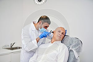 Doctor ENT checking ear with otoscope to man patient at hospital