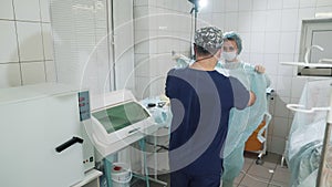 The doctor enters the operating room. A nurse helps to dress a doctor`s gown in the operating room. Preparing for