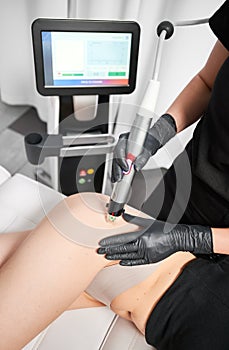 Doctor esthetician performing radiofrequency treatment on woman hip.