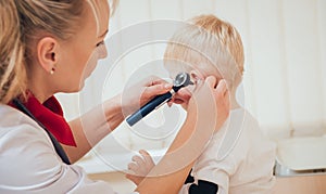 Doctor examines ear with otoscope in a pediatrician room.