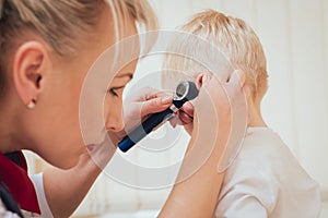 Doctor examines ear with otoscope in a pediatrician room.