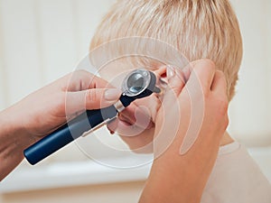Doctor examines ear with otoscope in a pediatrician room.