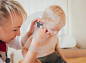 Doctor examines ear with otoscope in a pediatrician room.