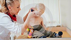 Doctor examines ear with otoscope in a pediatrician room.