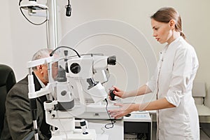 doctor examines elderly man& x27;s eye on screen of autorefractometer.