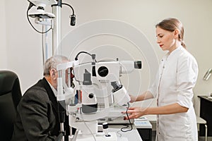 doctor examines elderly man's eye on screen of autorefractometer.