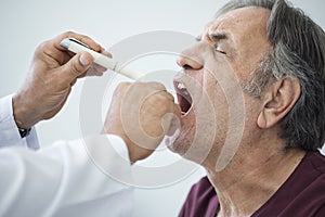 Doctor examines senior man for sore throat photo
