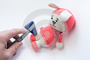 Doctor examines soft rabbit toy with neurological hammer and checks reflexes in feet. Concept for neurological examination of neur