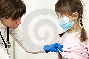 Doctor examining child girl covered with green rashes on face and stomach ill with chickenpox, measles or rubella virus