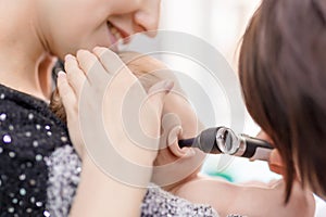 Doctor examining childs ear with otoscope. Mom holding baby with hands. Children healthcare and disease prevention