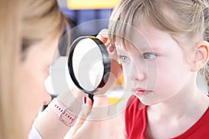 Doctor examining eye of little girl using magnifying glass