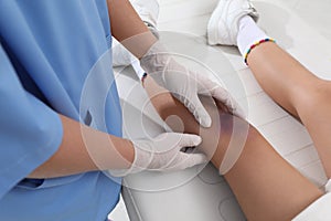 Doctor examining little child`s bruised knee in hospital, closeup