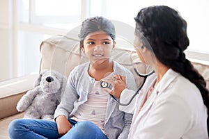 Doctor examining a little girl with stethoscope. Female paediatrician listening to childs heartbeat during home visit or