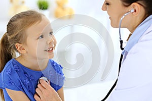 Doctor examining a little girl by stethoscope. Happy smiling child patient at usual medical inspection. Medicine and