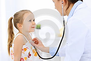 Doctor examining a little girl by stethoscope. Happy smiling child patient at usual medical inspection. Medicine and