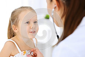 Doctor examining a little girl by stethoscope. Happy smiling child patient at usual medical inspection. Medicine and