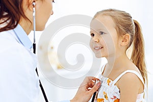 Doctor examining a little girl by stethoscope. Happy smiling child patient at usual medical inspection. Medicine and