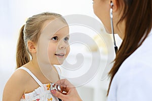 Doctor examining a little girl by stethoscope. Happy smiling child patient at usual medical inspection. Medicine and