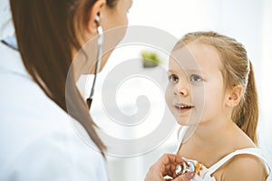 Doctor examining a little girl by stethoscope. Happy smiling child patient at usual medical inspection. Medicine and