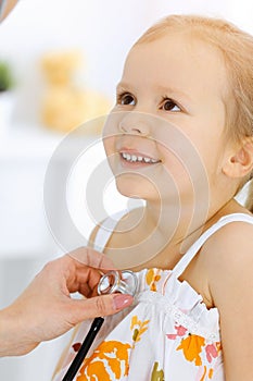 Doctor examining a little girl by stethoscope. Happy smiling child patient at usual medical inspection. Medicine and