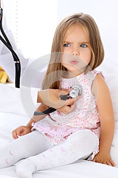 Doctor examining a little girl by stethoscope. Patient is in perplexity