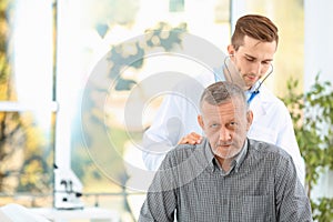 Doctor examining mature patient with stethoscope in hospital.