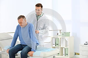 Doctor examining mature patient with stethoscope in hospital.