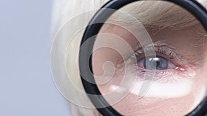 Doctor examining mature woman eyes through magnifying glass, ophthalmoscopy