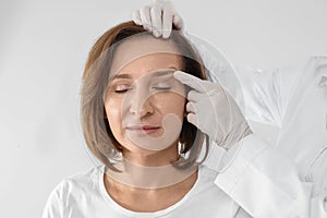 Doctor examining mature woman face before surgery on white background