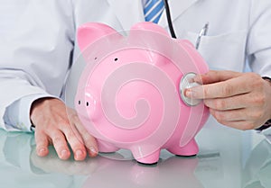 Doctor Examining Piggybank With Stethoscope