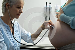 Doctor examining pregnant woman belly with stethoscope