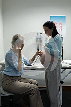 Doctor examining pregnant woman belly with stethoscope in examination room