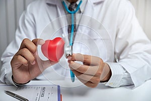 Doctor examining a red heart shaped ball with a stethoscope