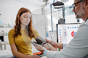 Doctor examining teenage girl, measuring blood pressure, using clinical blood pressure monitor. Concept of preventive