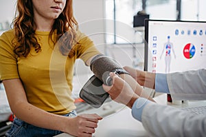 Doctor examining teenage girl, measuring blood pressure, using clinical blood pressure monitor. Concept of preventive