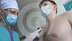 Doctor exams male patient with stethoscope looks for COVID-19 symptoms. Medic listens lungs of coughing man. Physician