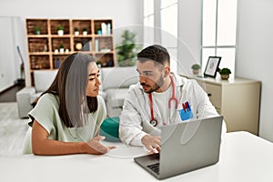 Doctor explain treatment to latin woman using laptop at clinic