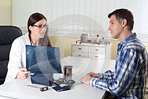 Doctor Explaining Lung X-ray Results to Middle Aged Patient in Consulting Room