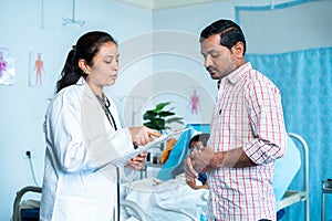 Doctor explaining patient health or medical report to worried father at hospital - concept of professional occupation