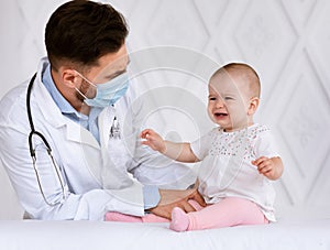Doctor In Face Mask Examining Little Baby Girl In Clinic