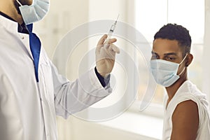 Doctor in face mask holding syringe before administering antiviral vaccine to patient