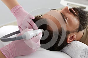 Doctor female dermatologist trichologist makes a procedure to stimulate hair growth on head to a patient man