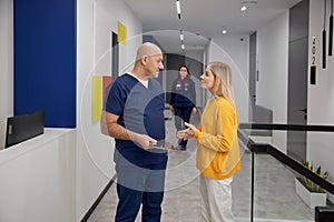 Doctor and female patient discussing something while standing in clinic corridor