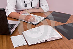 Doctor filling prescription with patient`s x-ray on wooden table