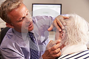 Doctor Fitting Senior Female Patient With Hearing Aid