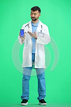 The doctor, in full height, on a green background, shows the phone