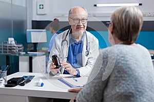 Doctor giving bottle of pills with medicine to old patient at meeting appointment in cabinet