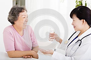 Doctor giving medication and water to senior woman