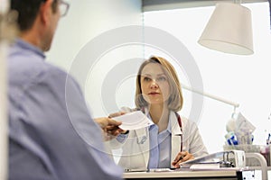 Doctor giving prescription to patient at desk in hospital
